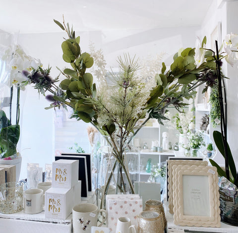 Large clear vase full of artificial flowers and eucalyptus